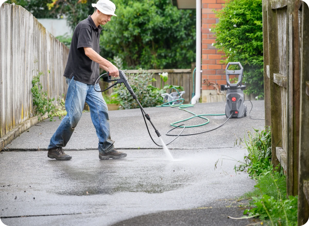 Man pressure washing a concrete driveway outside.