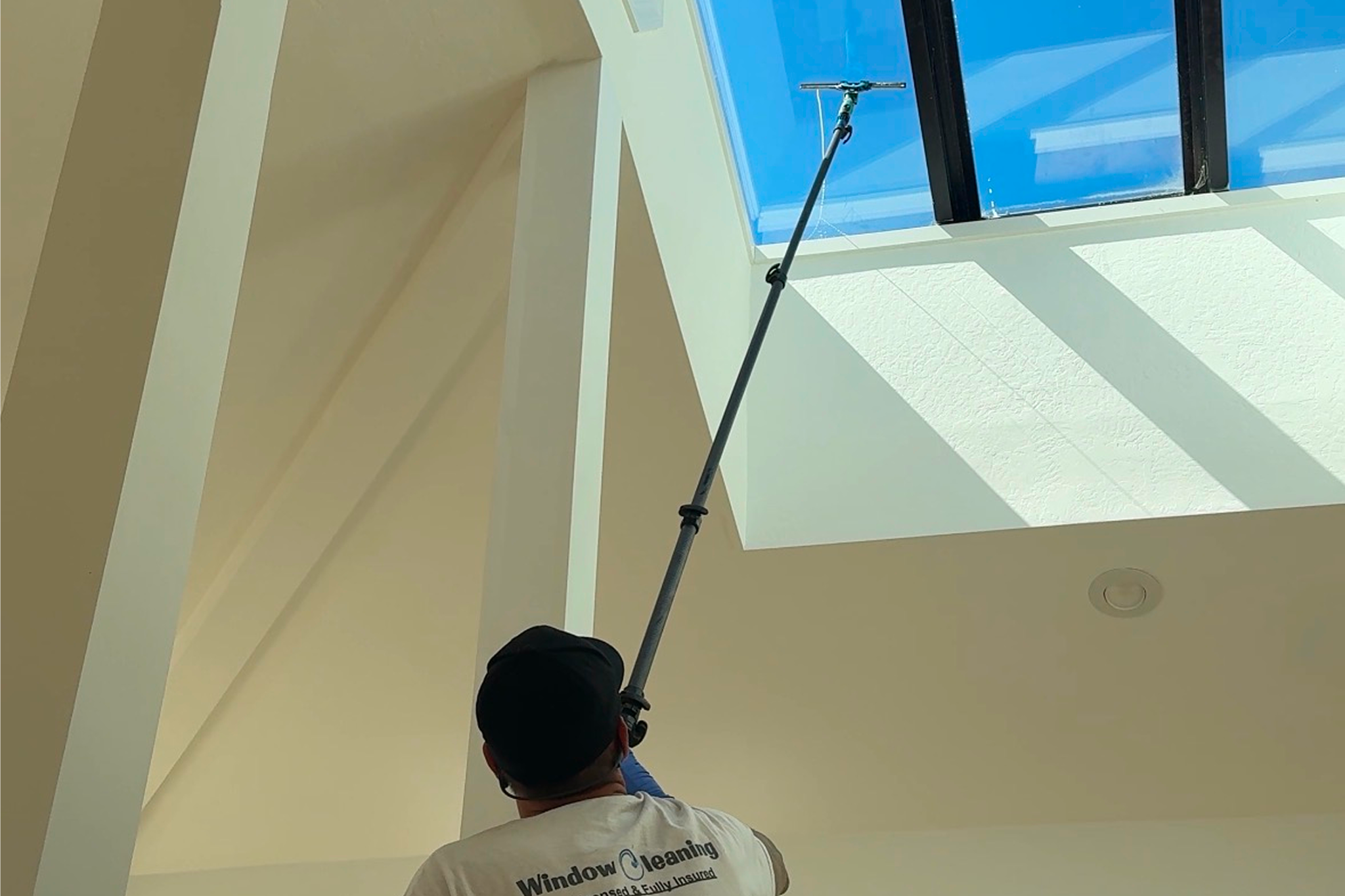 Person cleaning skylight with long pole.