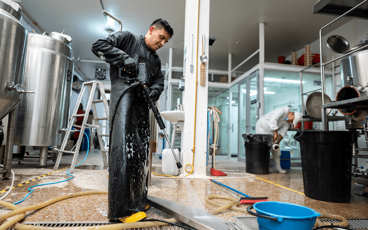 Worker cleaning industrial kitchen with hose.