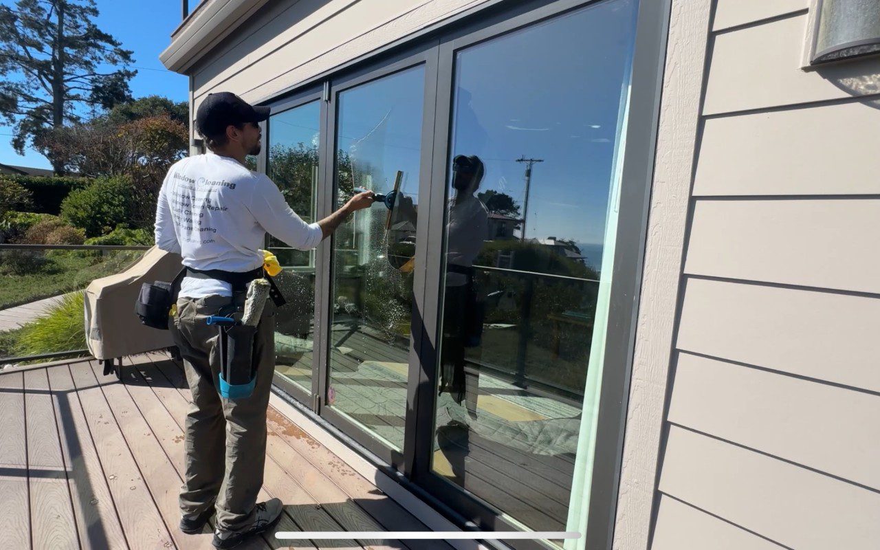 Person cleaning large glass sliding doors outside.