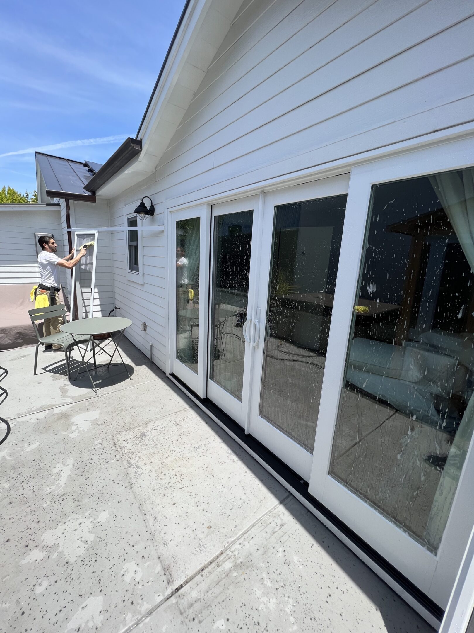 Person cleaning large glass doors outside house.