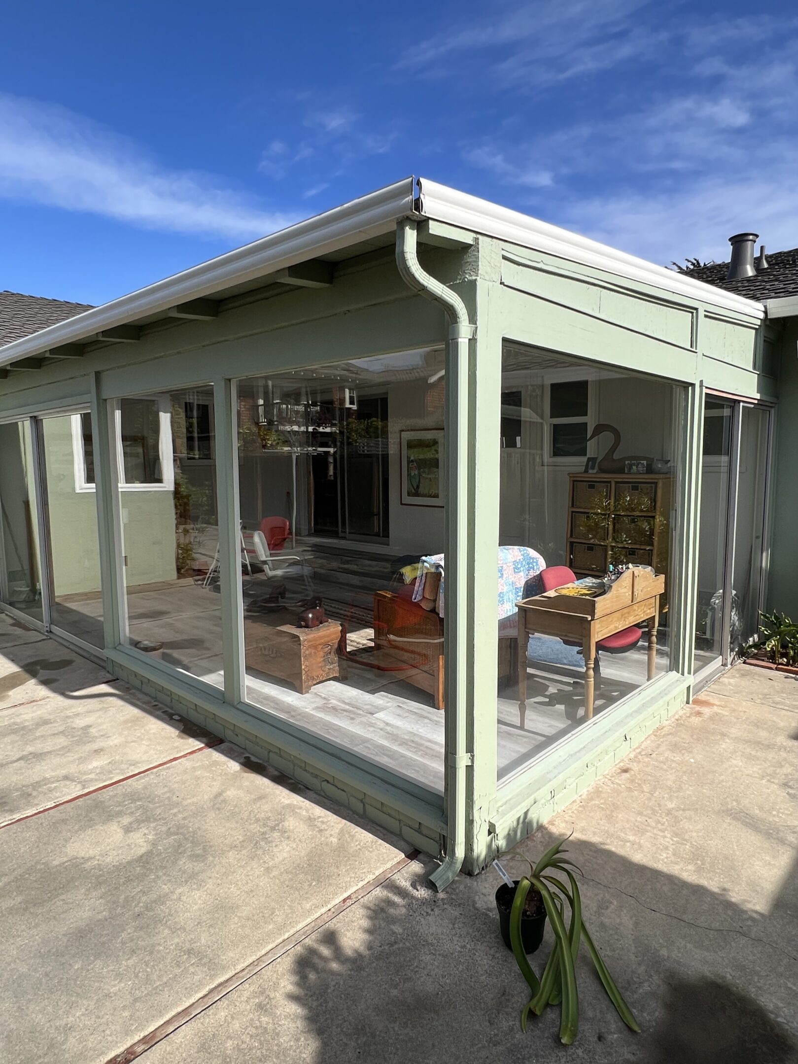 Green sunroom with glass walls and furniture.