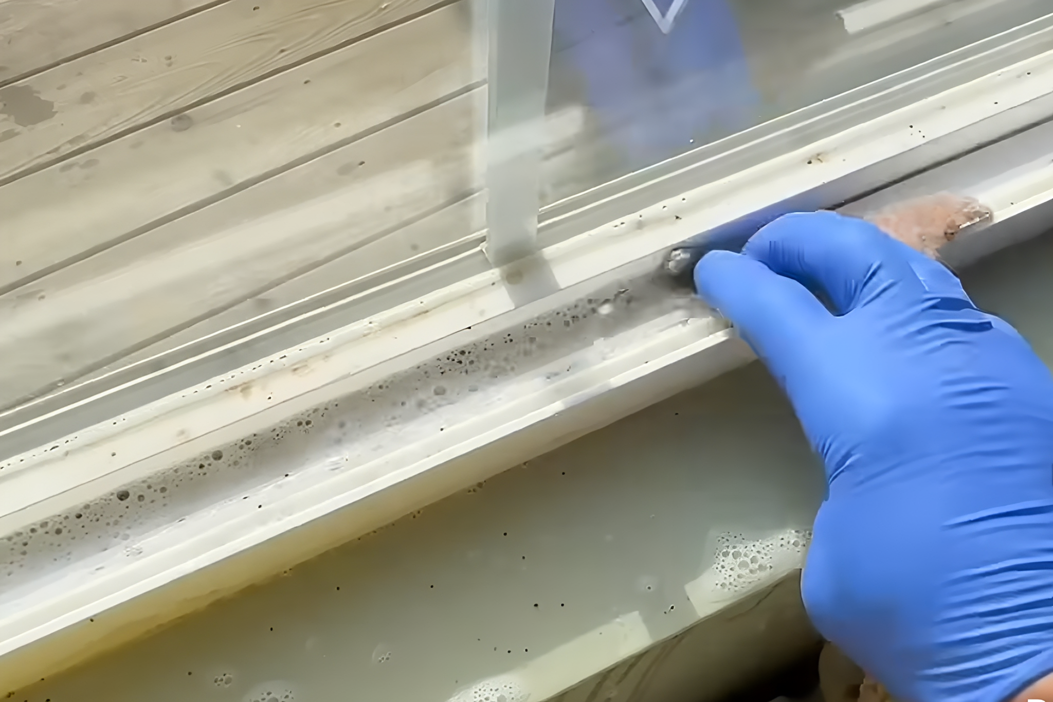 Cleaning window track with gloved hand.
